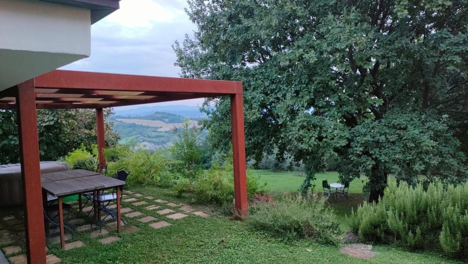 Un espace extérieur abrité, doté d’une table et de chaises, entouré de verdure et offrant une vue sur des collines lointaines.