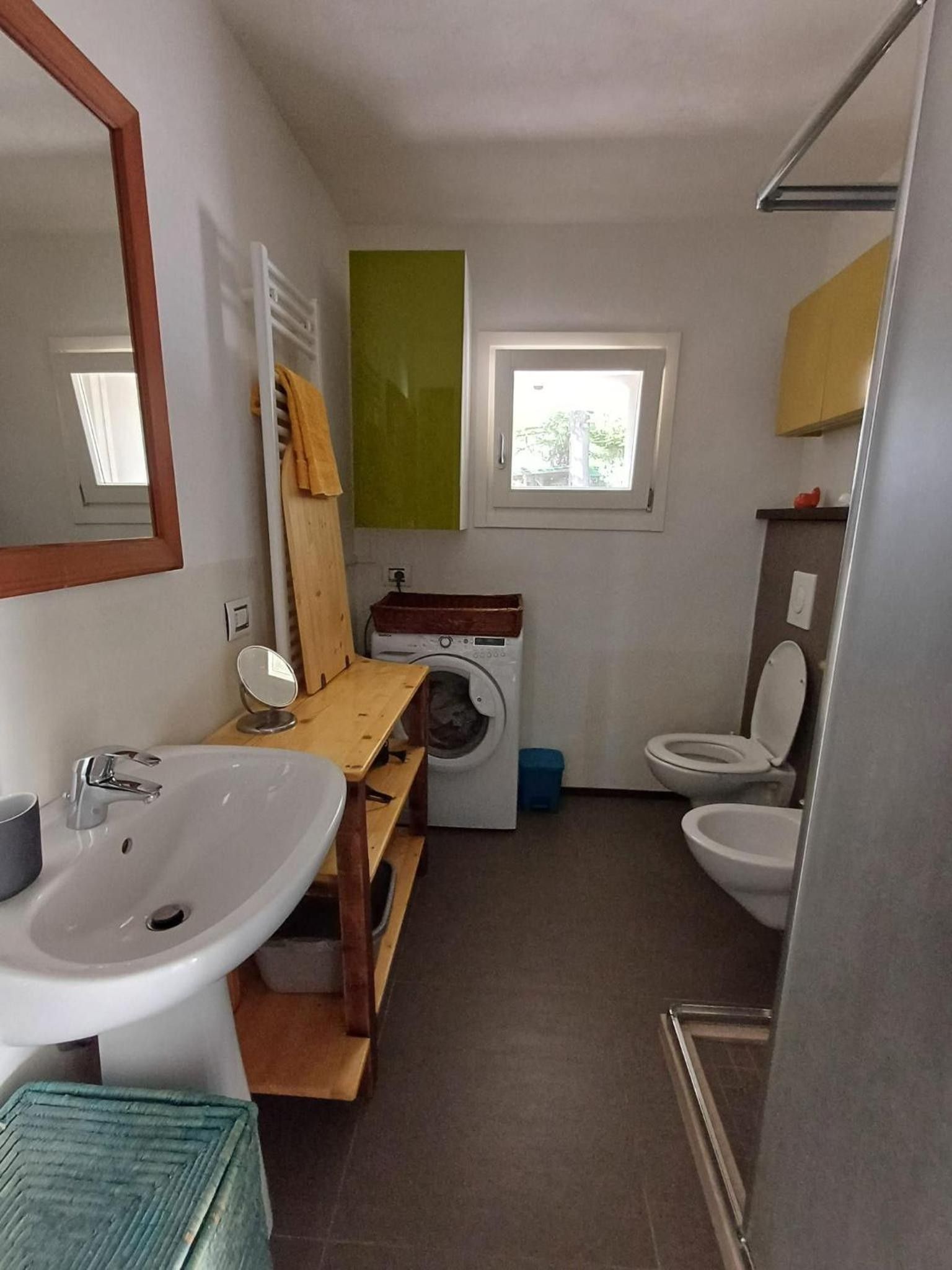A compact bathroom with a sink, mirror, toilet, and a washing machine.