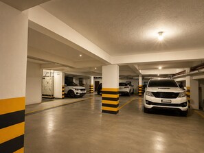A multi-level parking garage with white and yellow striped pillars, a white car in the foreground, and a white SUV in the background. - Hotel Iris Grand (Bengaluru)