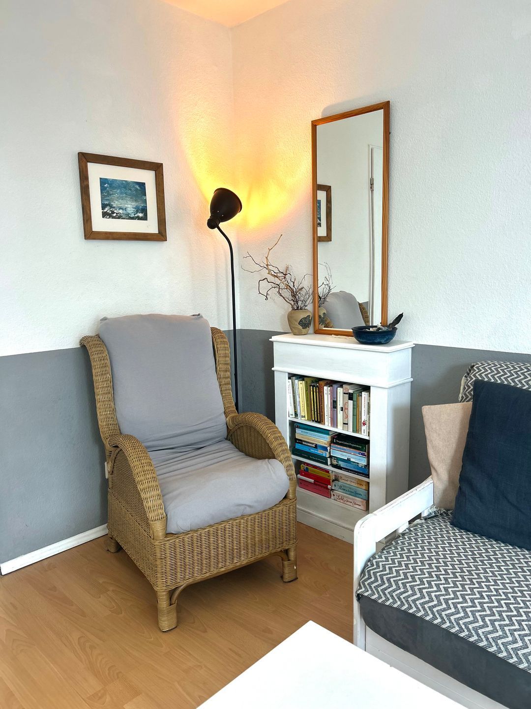 Ein Wohnzimmer mit einem Korbstuhl, einem Bücherregal, einem Spiegel und einer Lampe.