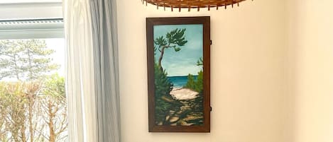 A room with a white radiator, a wicker basket on a shelf, a painting of a beach, and a table with a black vase.