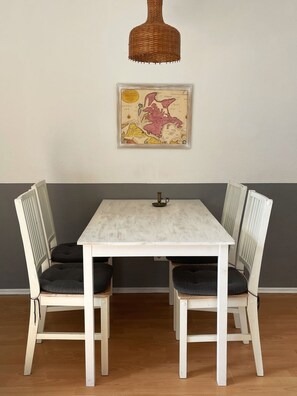A dining table with four chairs, a hanging light fixture, and a framed map on the wall. - Seeschwalbe 2 Vacation Rental - Small Terrace Apartment - Ideal for a Beach Vacation (Breege)