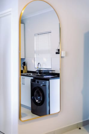 A modern kitchen with a built-in washing machine, a sink, and a window with blinds.