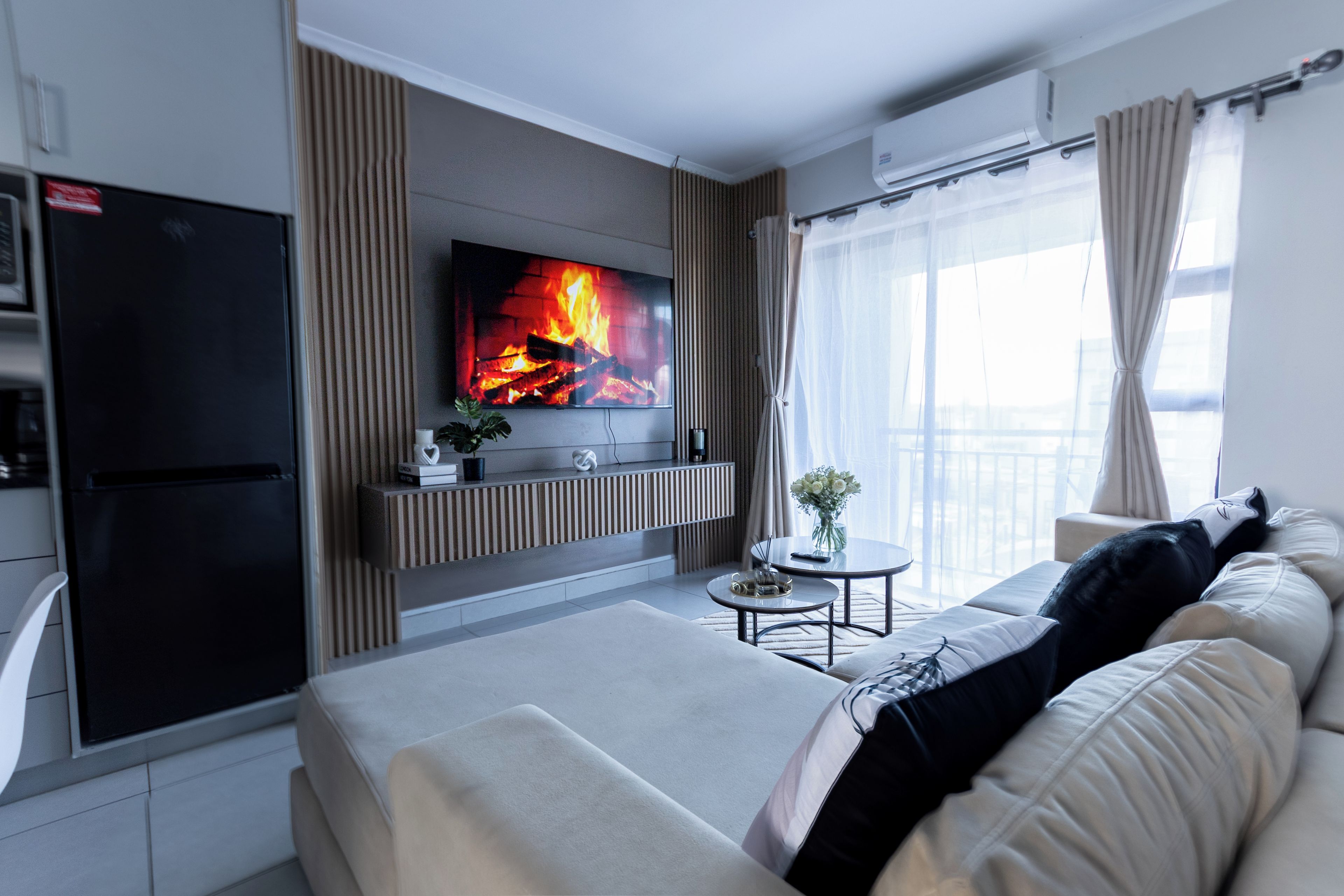 A modern living room with a flat-screen TV mounted on the wall, a sofa, a coffee table, and a dining table.