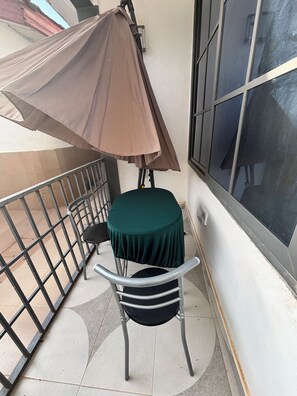Un petit balcon avec une table et des chaises, une rambarde en métal et une grande fenêtre.