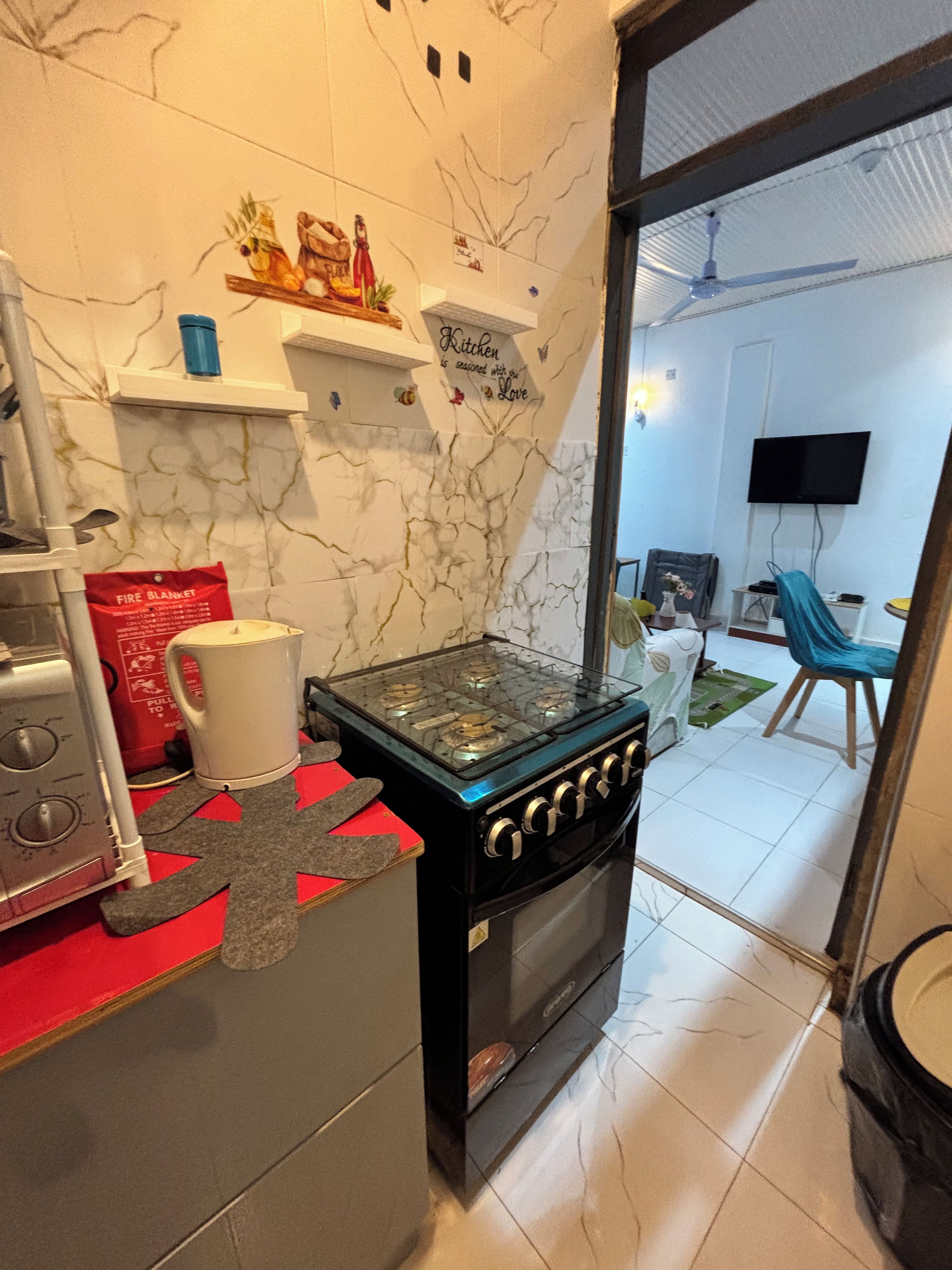 A kitchen with a gas stove, a coffee maker, and a red fire blanket on the counter.