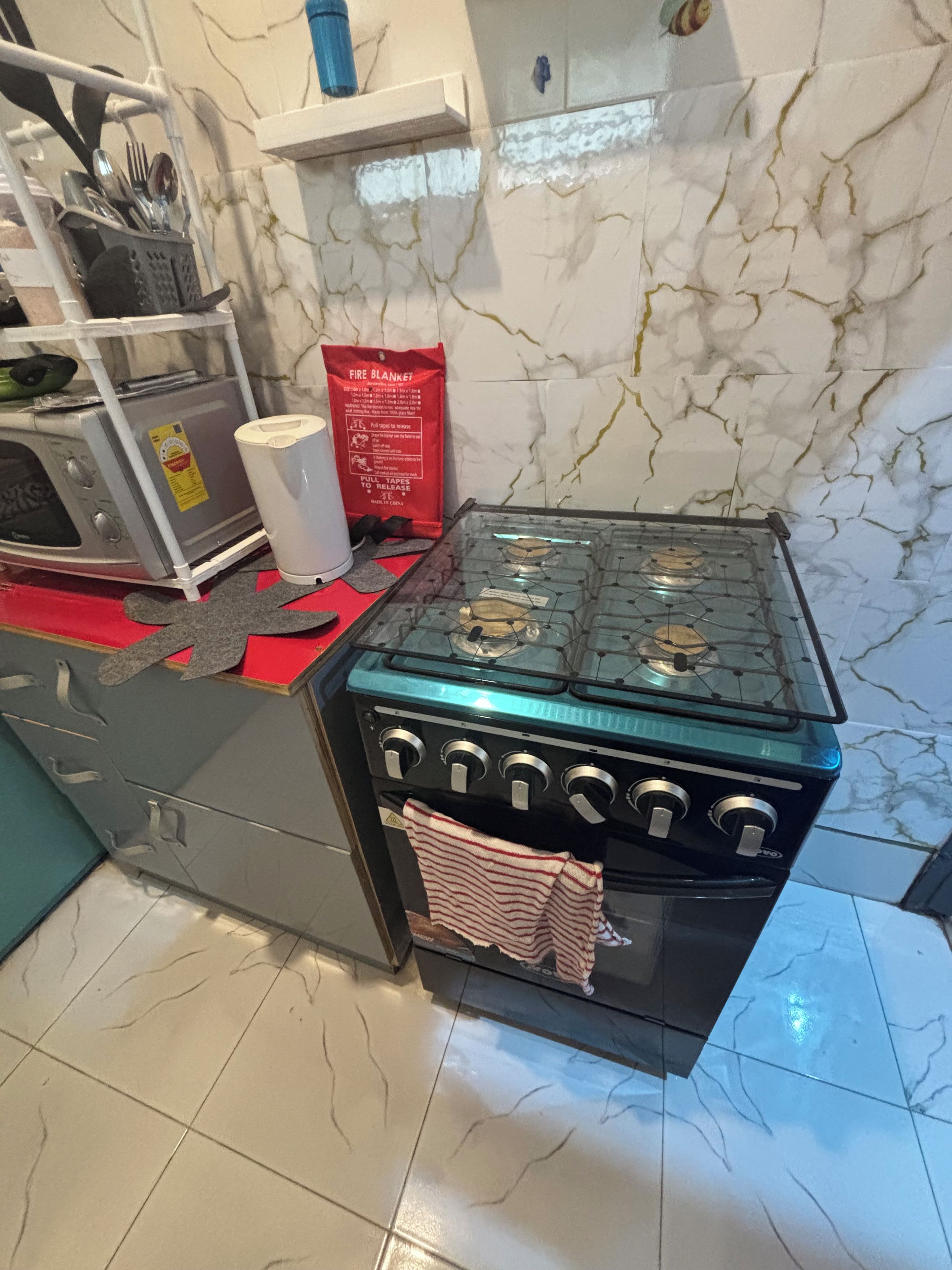 A kitchen with a gas stove, a microwave, and a red fire blanket on the counter.