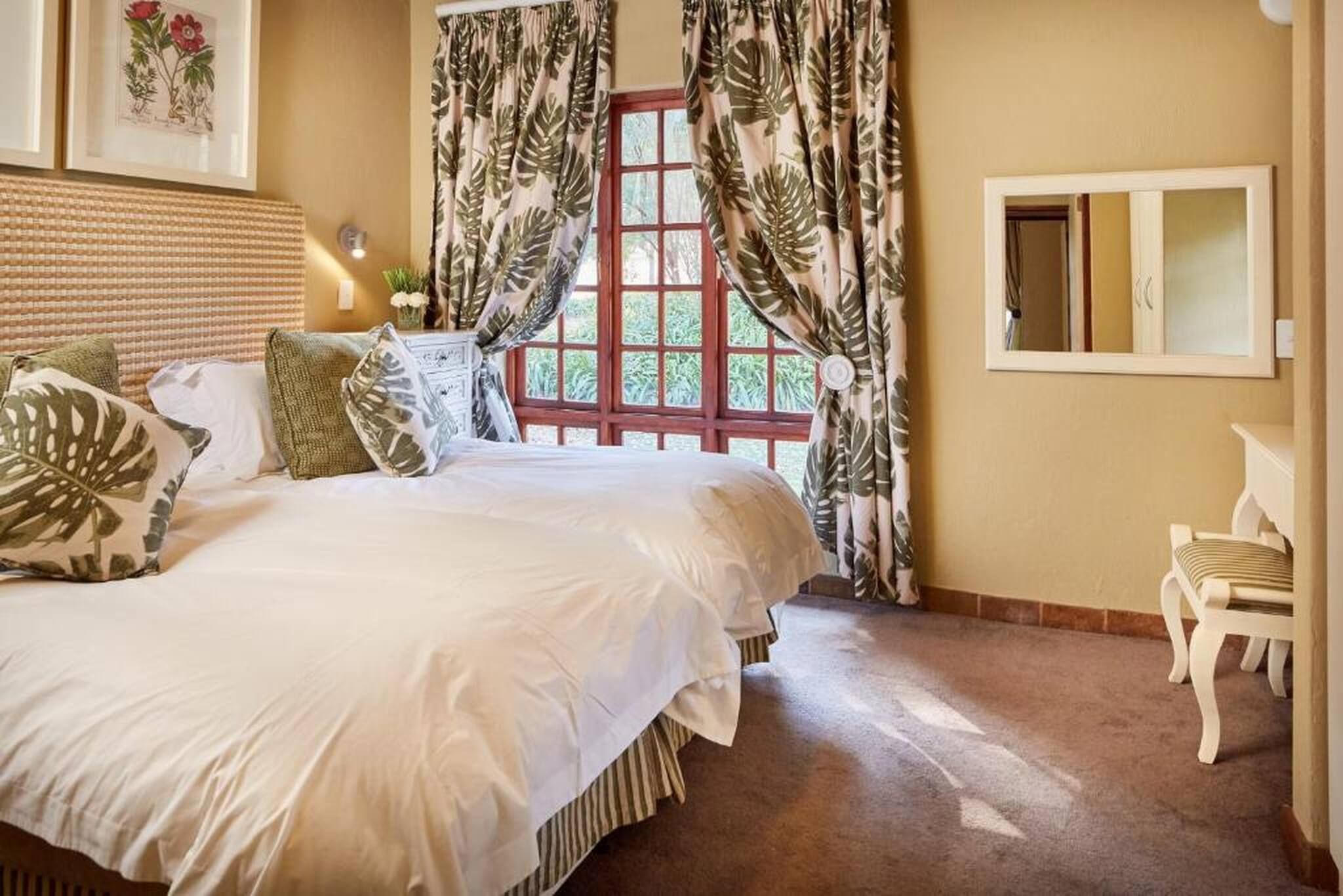 Een slaapkamer met een groot bed, een raam met gordijnen, een nachtkastje en een spiegel.