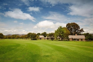 A golf course with a clear sky, a well-maintained lawn, and several buildings in the distance. - Magalies Park Resort 2-bedroom WBT Rentals (Hartbeespoort)