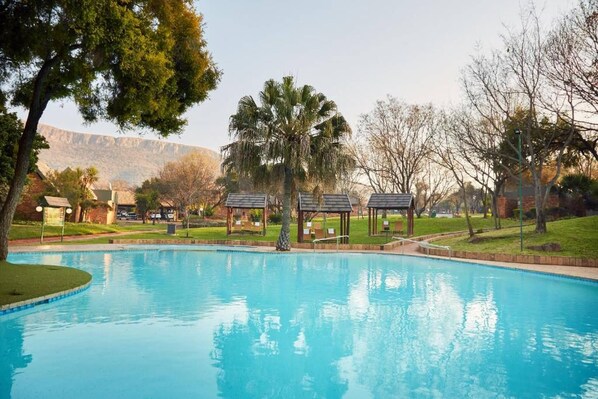 A swimming pool with a surrounding grassy area, trees, and a mountain in the background.