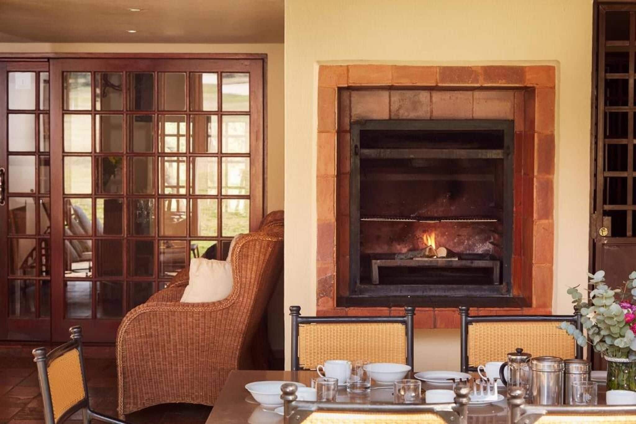 Un comedor con chimenea, muebles de mimbre y una mesa dispuesta para una comida.