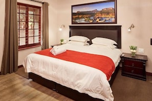 Une chambre d’hôtel avec un grand lit, un tableau au-dessus du lit, une table de chevet et une fenêtre avec des rideaux.
