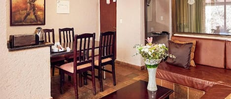 A living room with a brown sofa, a coffee table, a dining table with chairs, and a painting on the wall.