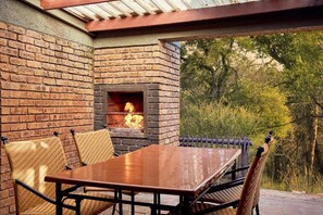 An outdoor patio with a brick fireplace, a wooden table, and wicker chairs.