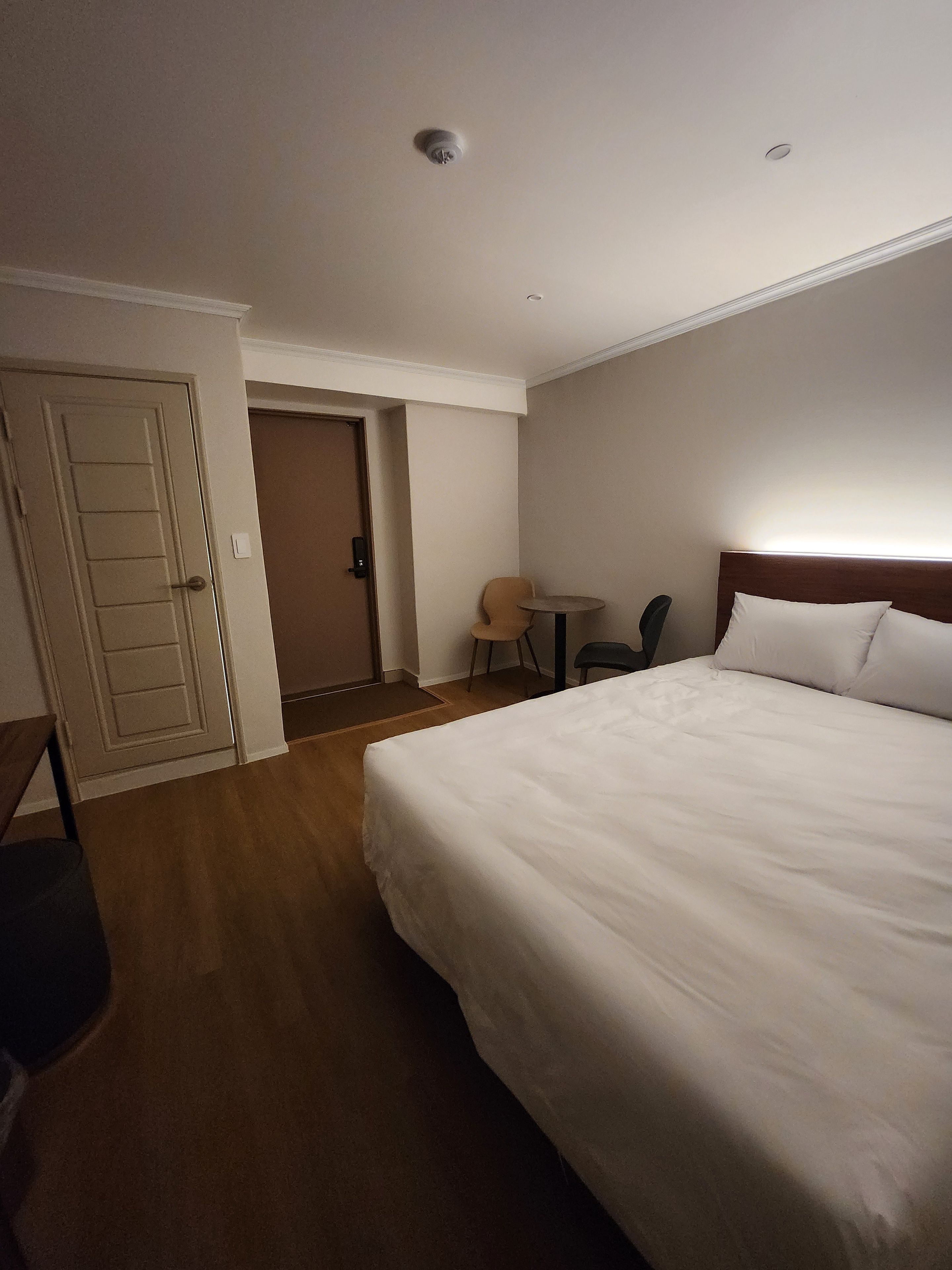 A hotel room with a large bed, a desk, a chair, and a door.