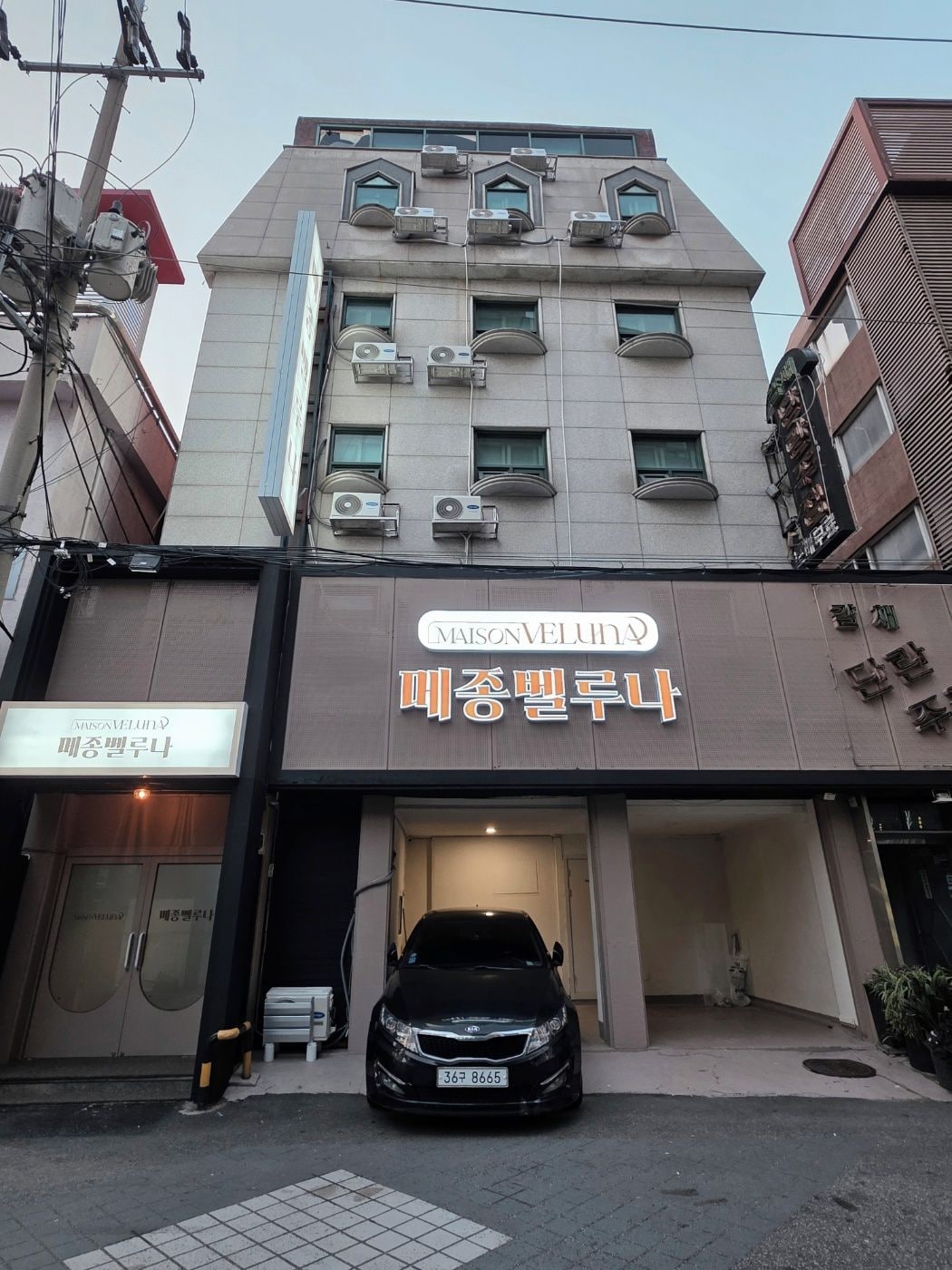A building with a sign for 'MAISON VELU' and a car parked in front.