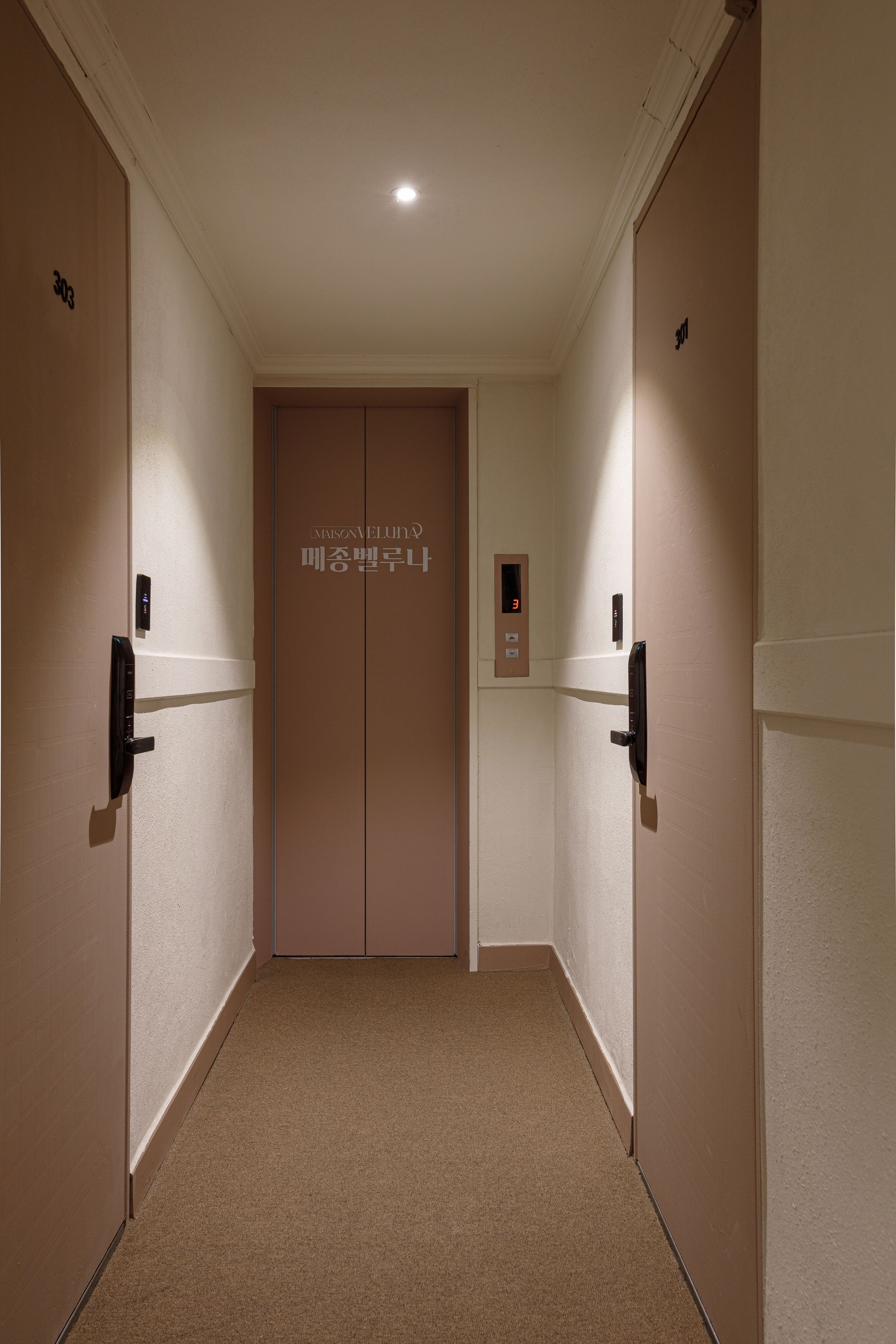 A hallway with two doors, each marked with a number. There is a digital elevator control panel above the doors.