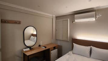 A hotel room with a bed, a desk, a mirror, a wall-mounted air conditioner, and a window with blinds.