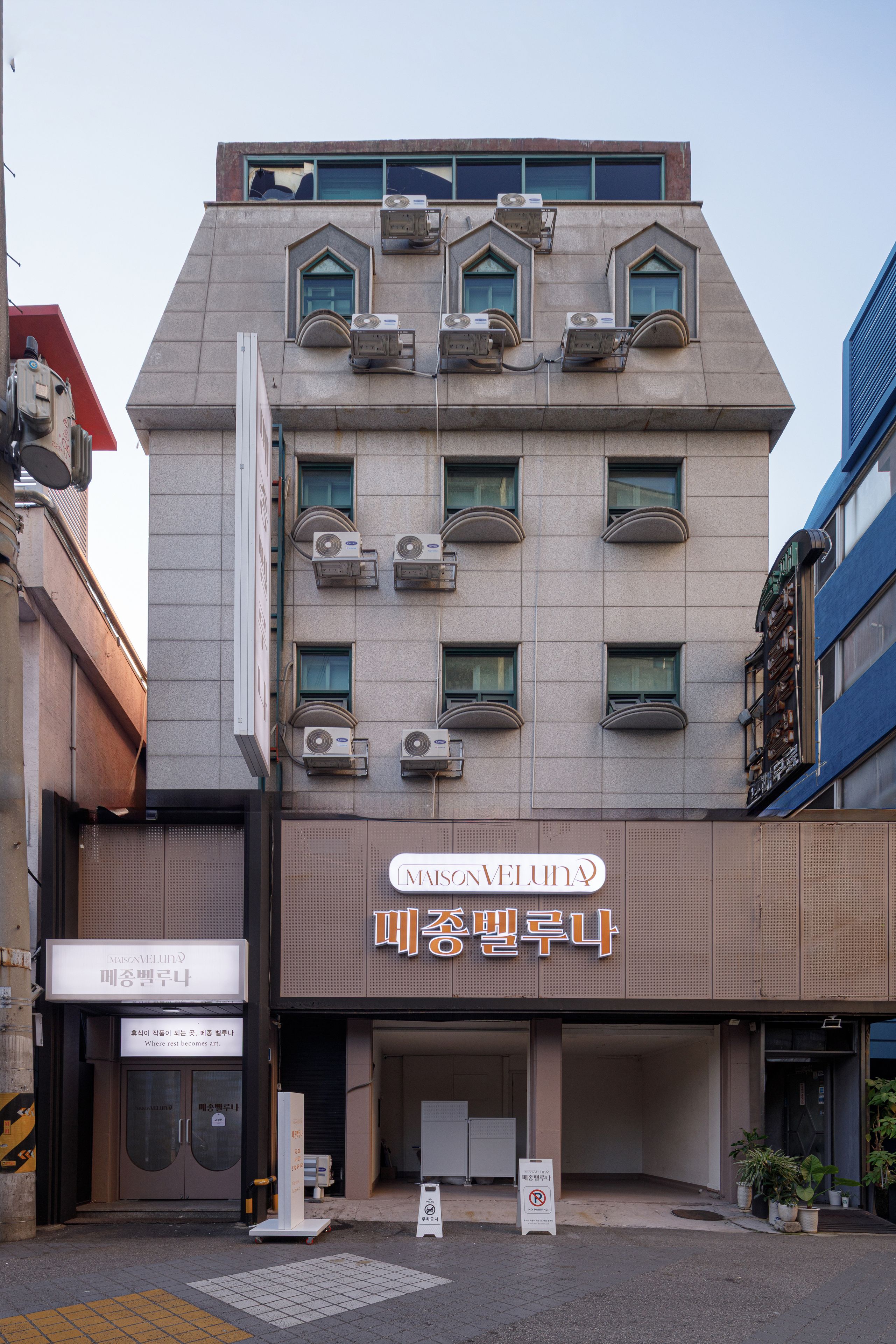 A building with multiple air conditioning units, a storefront with signage, and a gated entrance.