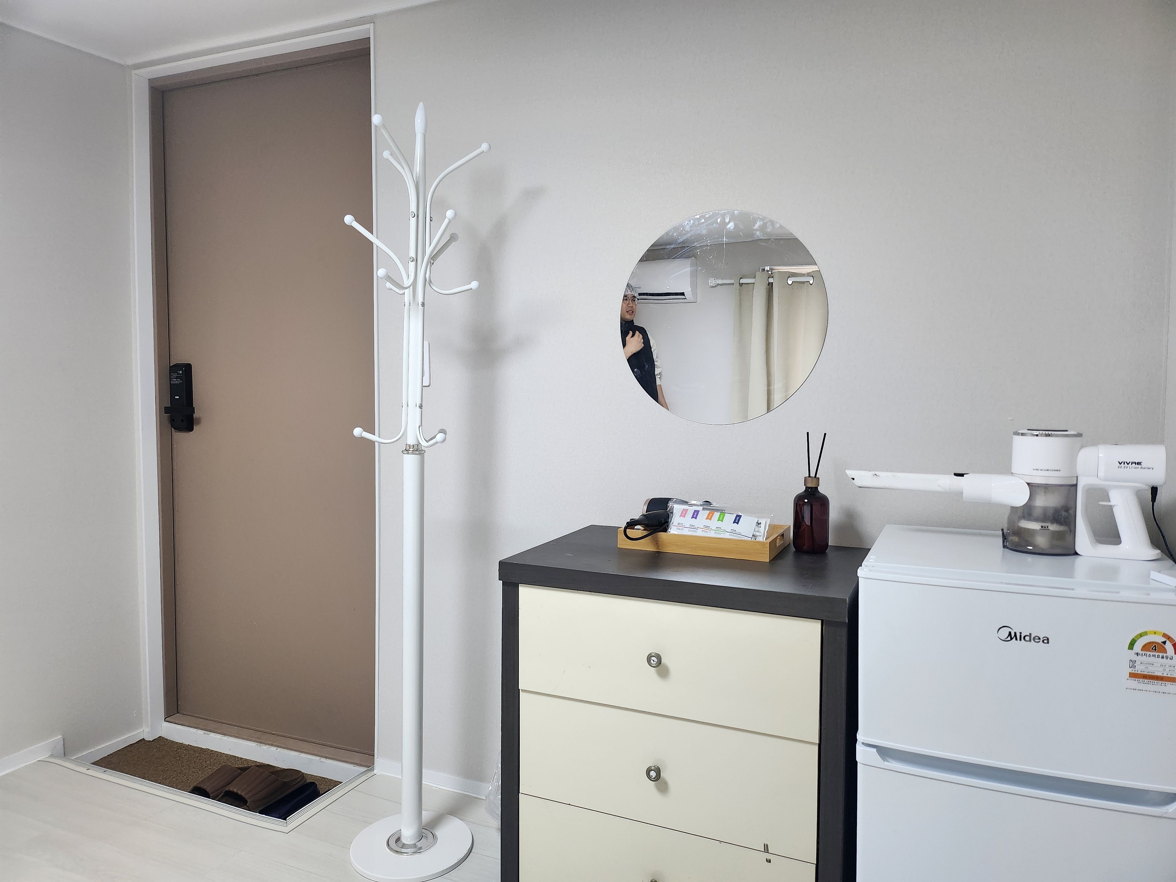 A room with a coat rack, a mirror, a minibar, and a small table with a coffee machine.