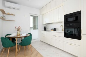 A modern kitchen with white cabinetry, a black oven, and a dining area with green chairs and a round table. - Warsaw | Jagiellońska 79 | Stylish Studio | Balcony (Warszawa)
