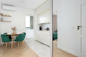 A modern kitchen with white cabinets, a dining area with a table and chairs, and a view to a balcony. - Warsaw | Jagiellońska 79 | Stylish Studio | Balcony (Warszawa)