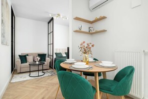 Un saló modern amb un sofà, una taula de dinar preparada per a quatre i una cadira tapissada de verd.