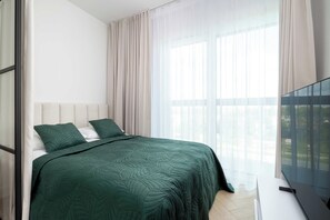 Een moderne slaapkamer met een bed, gordijnen en een televisie.