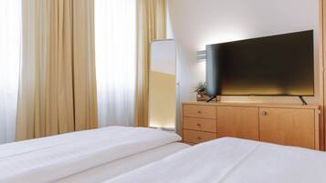 Une chambre d’hôtel avec un lit, un téléviseur posé sur un meuble en bois et une grande fenêtre avec des rideaux.