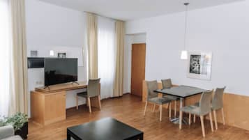 A modern living room with a flat-screen TV, wooden furniture, a dining table with chairs, and a small coffee table.
