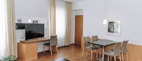 A modern living room with a flat-screen TV, wooden furniture, a dining table with chairs, and a small coffee table.