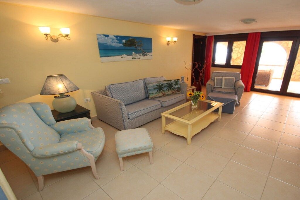 Un salon comprenant un canapé, un fauteuil, un pouf, une table basse et un tableau accroché au mur.