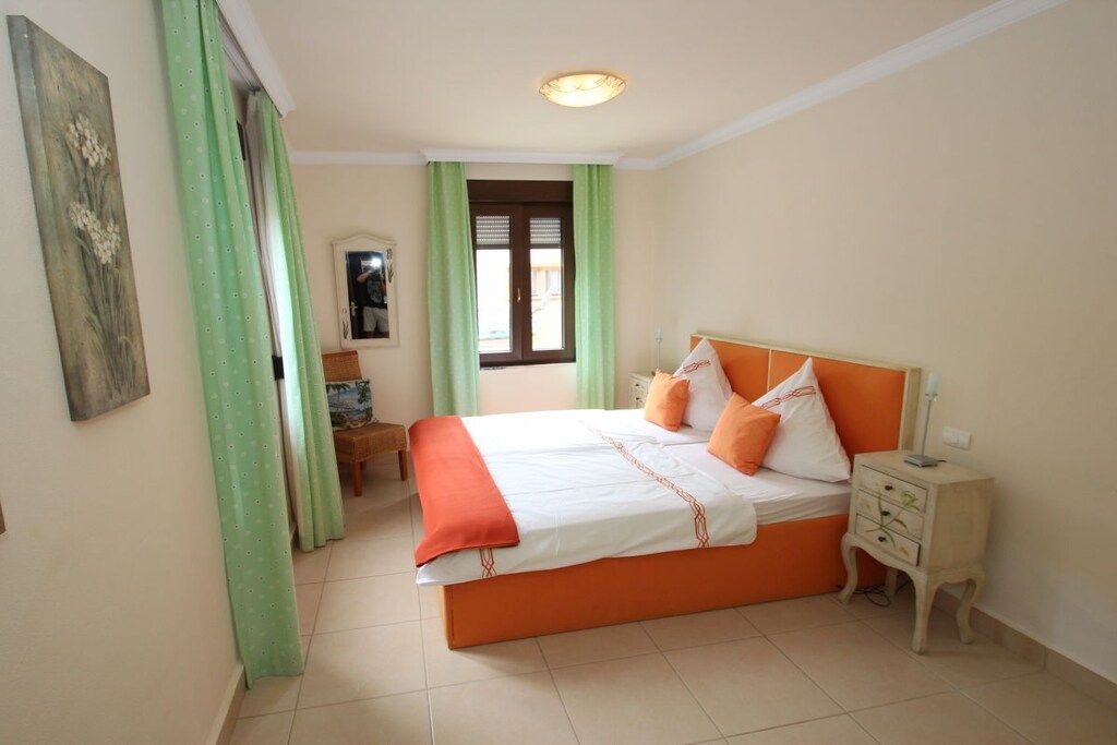 A bedroom with a large bed, a nightstand, a window with curtains, and a painting on the wall.