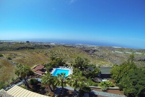 Ein Resort mit Swimmingpool, umgeben von Palmen, vor einer Küstenlandschaft.