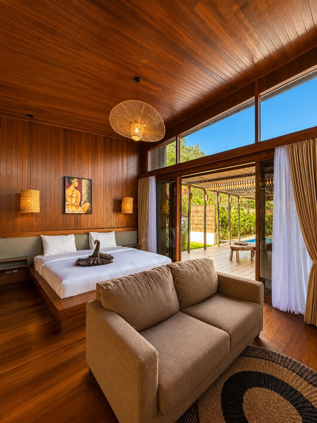A bedroom with a large bed, a sofa, and a view of a pool through glass doors.
