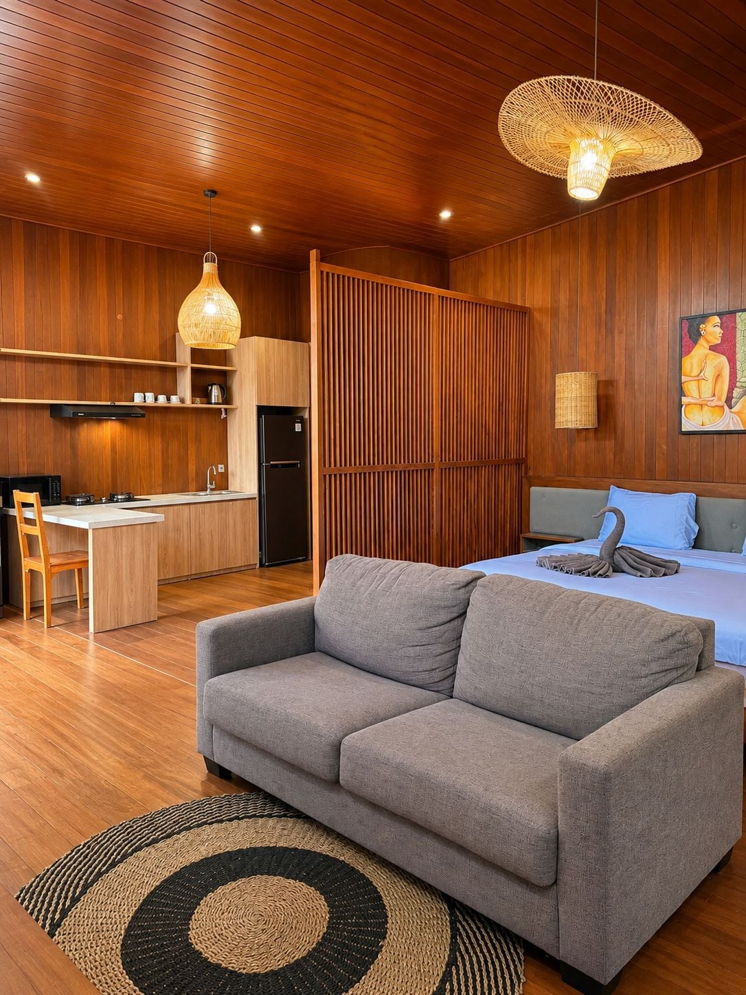 A modern interior with a sofa, a bed with a swan-shaped pillow, a kitchen area, and a wooden ceiling.