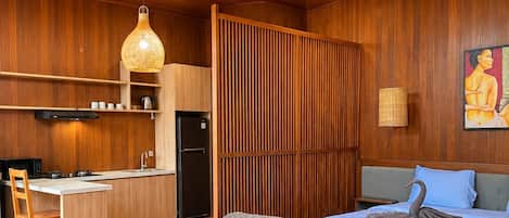 Un interior moderno con sofá, cama con almohada con forma de cisne, zona de cocina y techo de madera.