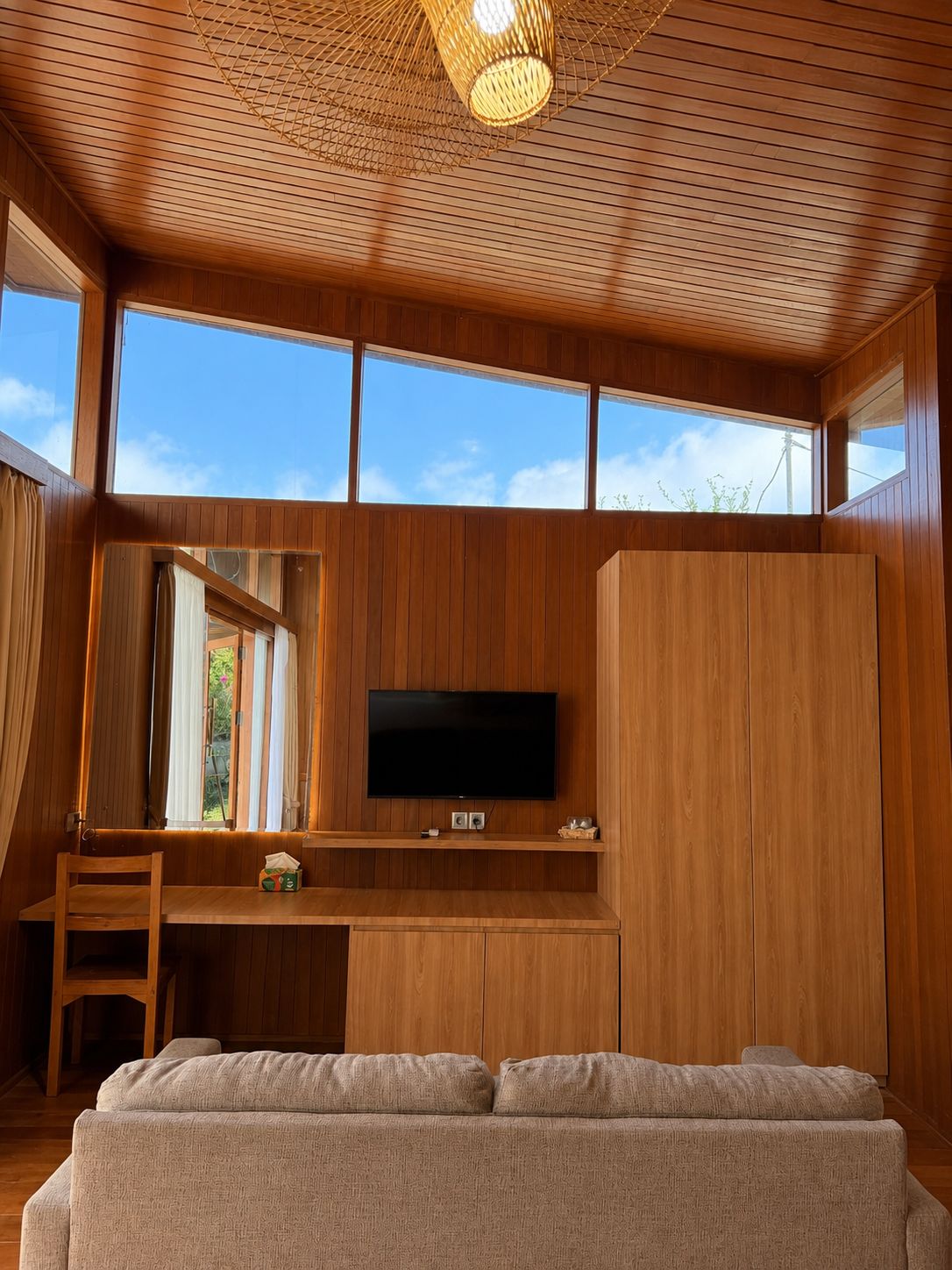 Une pièce dotée d’un plafond en bois, d’un téléviseur à écran plat fixé au mur, d’un bureau en bois, d’un canapé confortable et de grandes fenêtres.