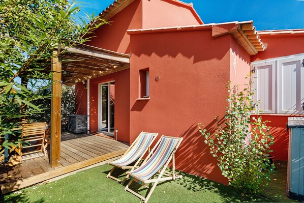 Un bâtiment rouge doté d’une terrasse en bois et de deux chaises longues à rayures.