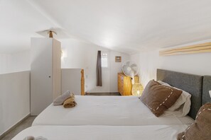 Une chambre à coucher comprenant un lit, une commode, un ventilateur et une porte donnant sur une autre pièce.