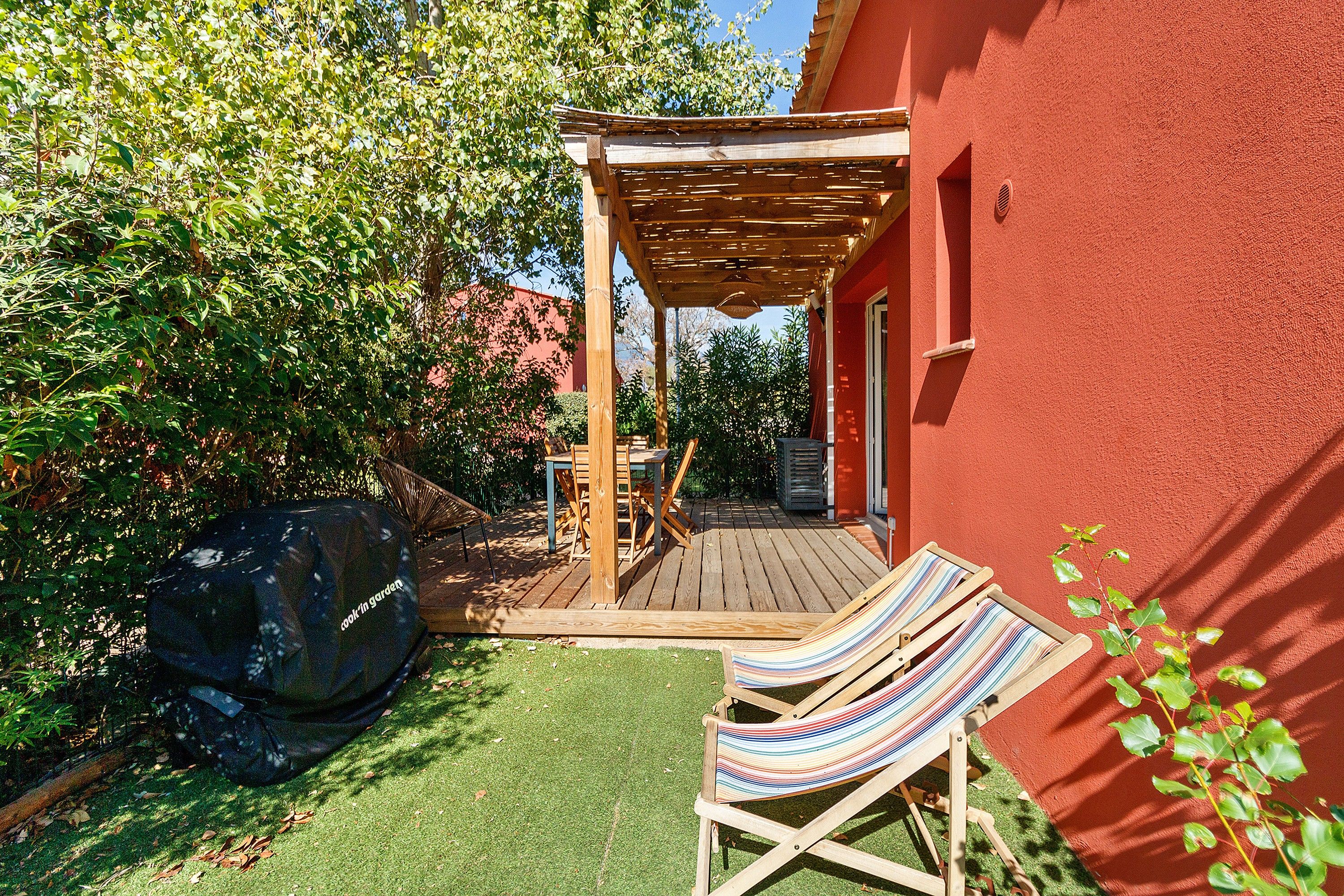 Un patio in legno con una pergola, un barbecue e due comode poltrone a righe.