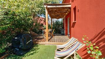 Un patio in legno con una pergola, un barbecue e due comode poltrone a righe.