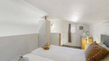 A hotel room with a bed, a bedside table, a mirror, a fan, and a window.