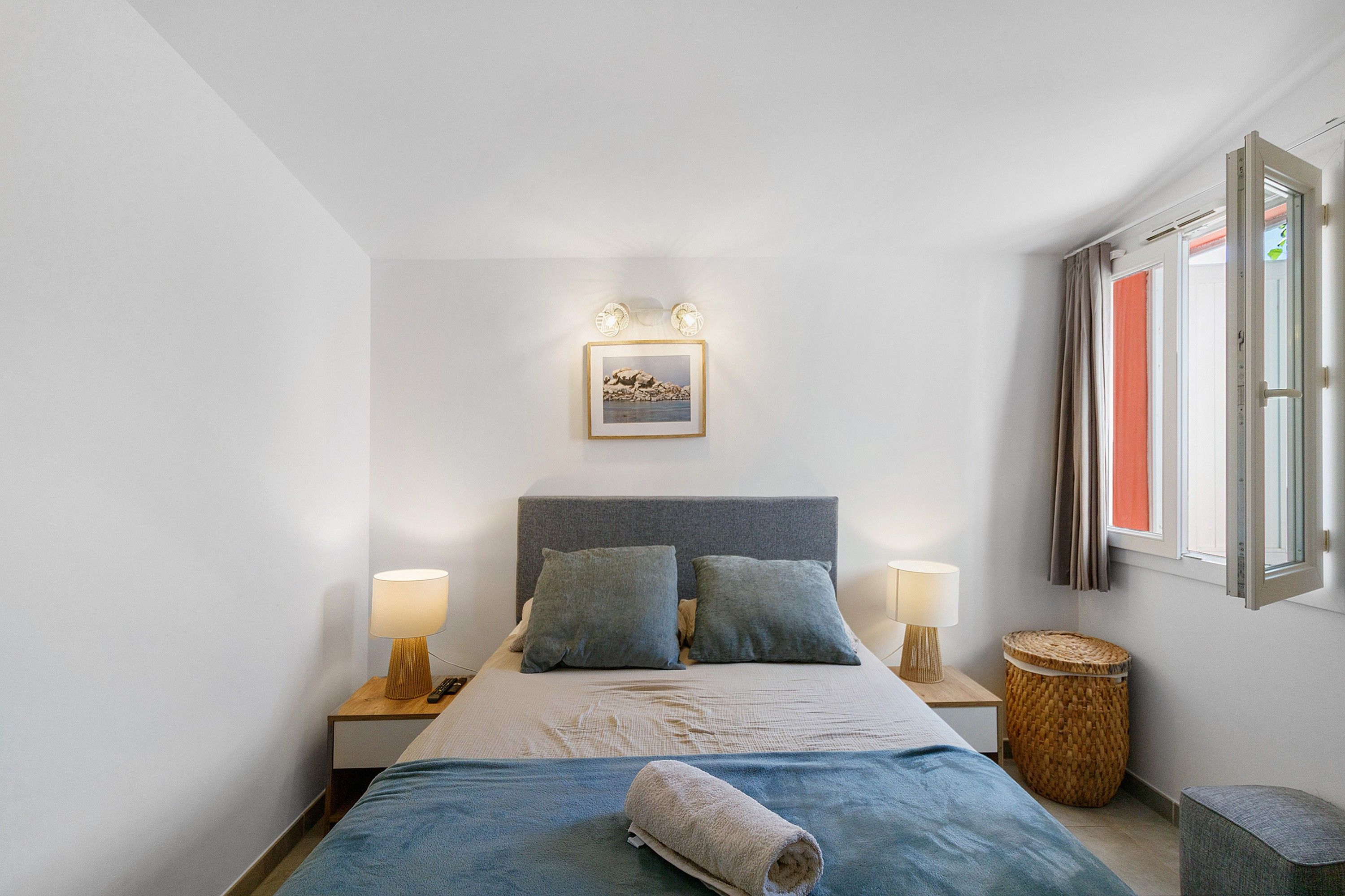Une chambre à coucher avec un lit, deux lampes de chevet, un tableau encadré et une fenêtre avec des rideaux.