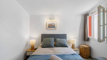 Une chambre à coucher avec un lit, deux lampes de chevet, un tableau encadré et une fenêtre avec des rideaux.
