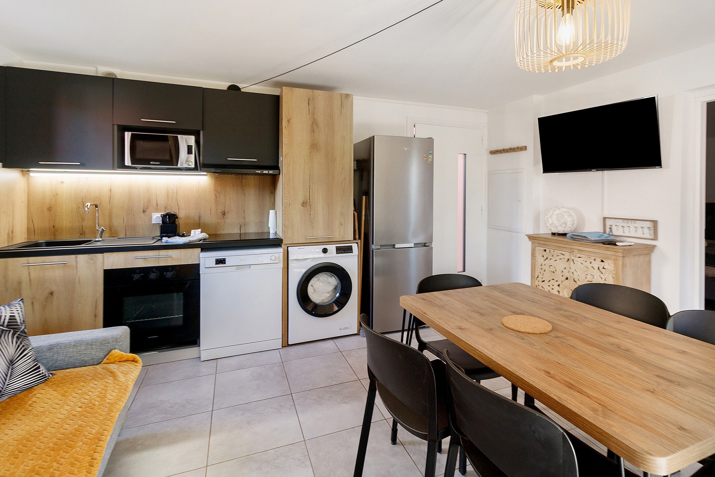 A compact kitchen with a microwave, oven, washing machine, and refrigerator. There's a dining area with a table and chairs.