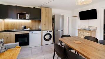 A compact kitchen with a microwave, oven, washing machine, and refrigerator. There's a dining area with a table and chairs.