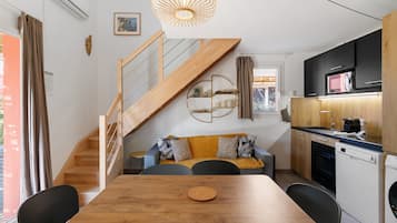A compact kitchen with modern appliances, a dining area with a wooden table, and a staircase leading to an upper level.