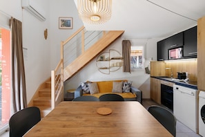 A compact kitchen with modern appliances, a dining area with a wooden table, and a staircase leading to an upper level. - Villa Sylody: mountain view, Wi-Fi, air conditioning, near San Ciprianu beach (Lecci)