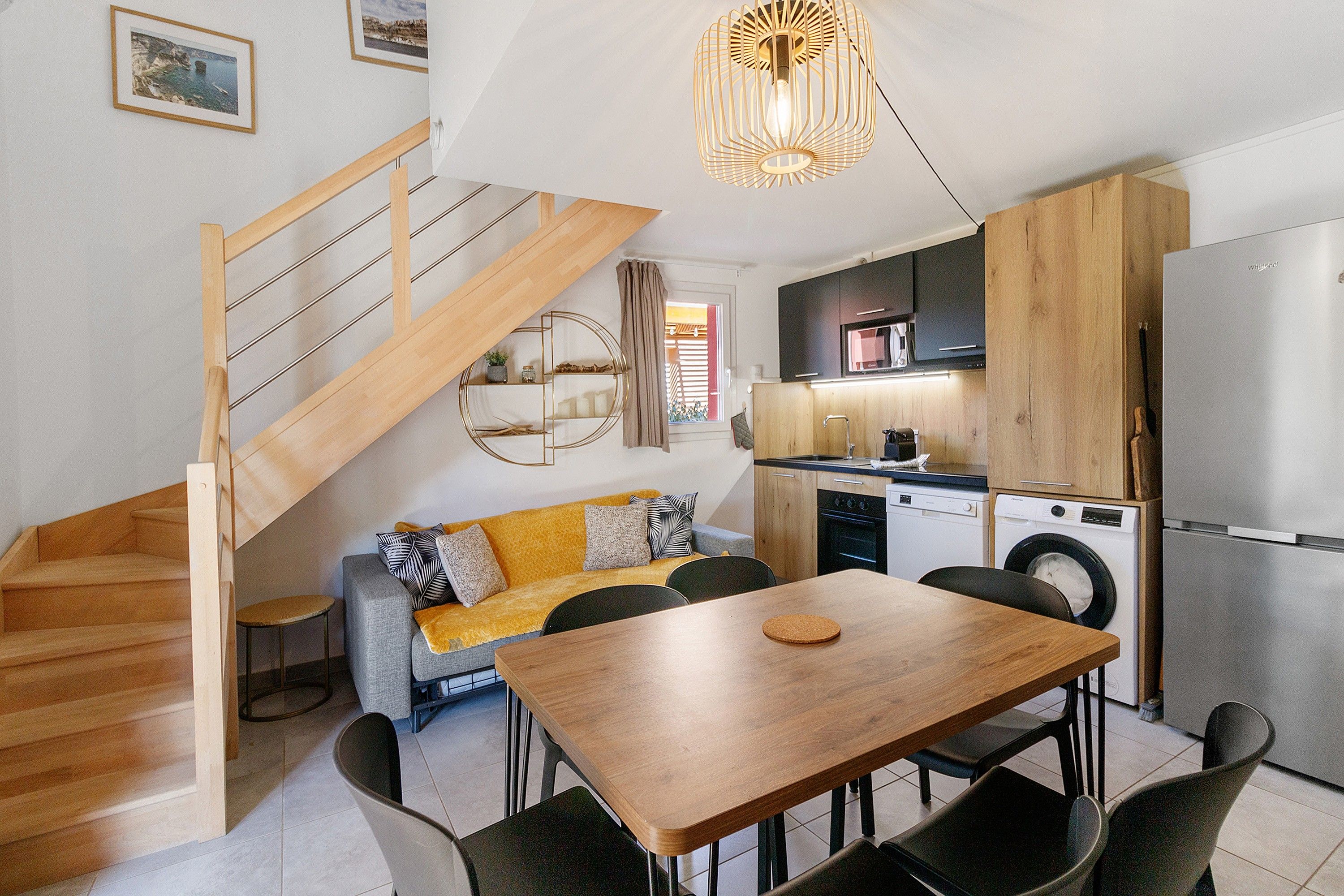 Una cucina moderna con una scala in legno, una zona pranzo con tavolo in legno e un divano con cuscini.